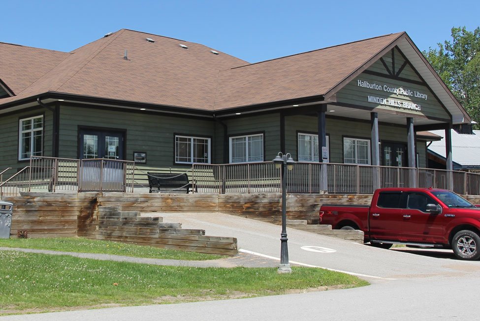 Exterior photo of the minden hills library on a sunny day with vehicles parked outside